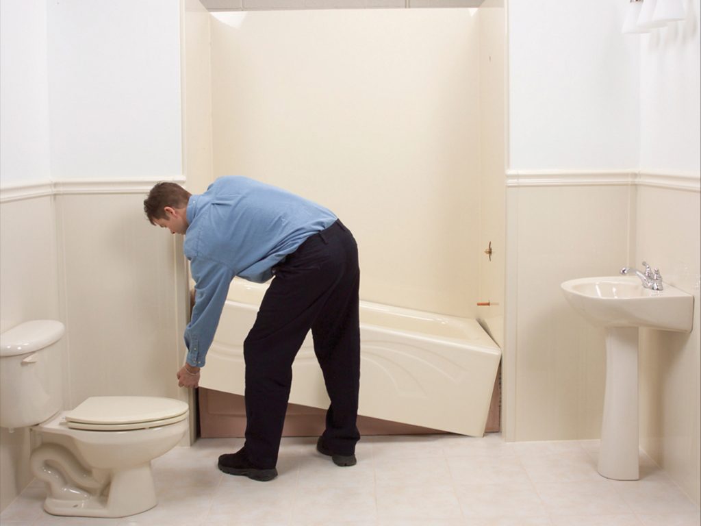 A man installing a bathtub in a bathroom.