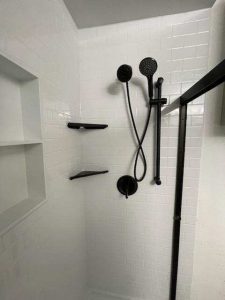 Black shower head and fixtures in tiled shower enclosure. For bathroom remodeler near me.