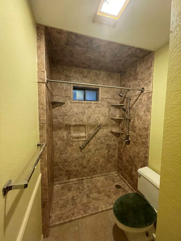 A bathroom with a tan shower and a toilet.