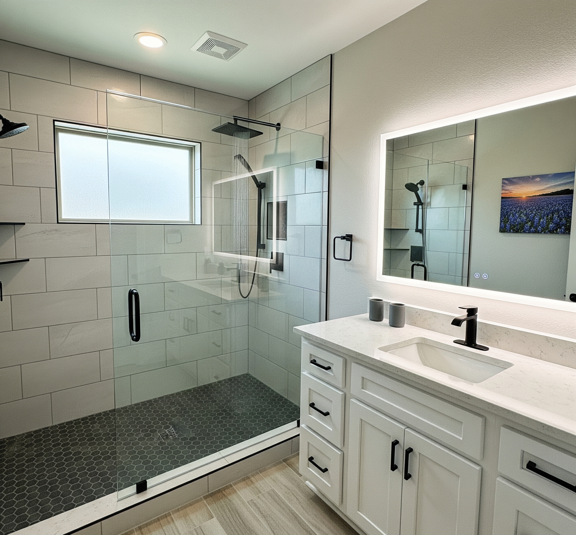 A modern bathroom remodel in a Kaufman County, Texas home, featuring a new walk-in shower with light gray subway tiles and a dark gray hexagon tile floor, a glass enclosure, a new white vanity with a quartz countertop, and a large mirror with built-in LED lighting by Affordable 1 Day Baths
